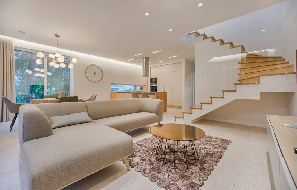 Bedrijfsafval Contemporary living room with neutral tones, a sleek sofa, and elegant wooden staircase.