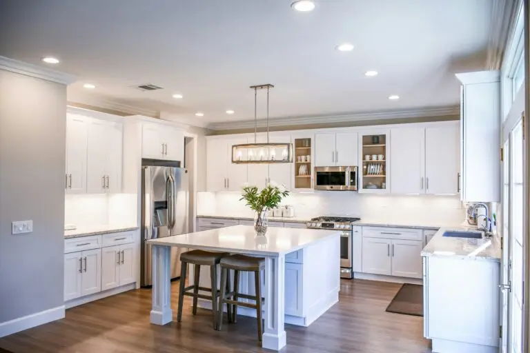 Bedrijfsafval Elegant white kitchen featuring an island, modern appliances, and ample natural light.